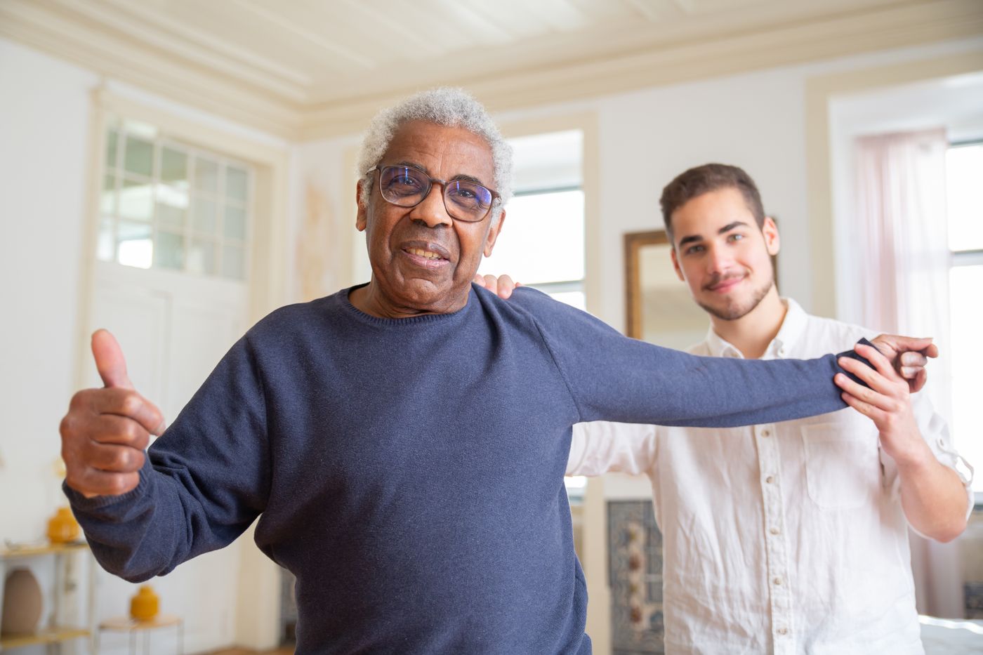 A smiling older man doing arm exercises with his caregiver at home