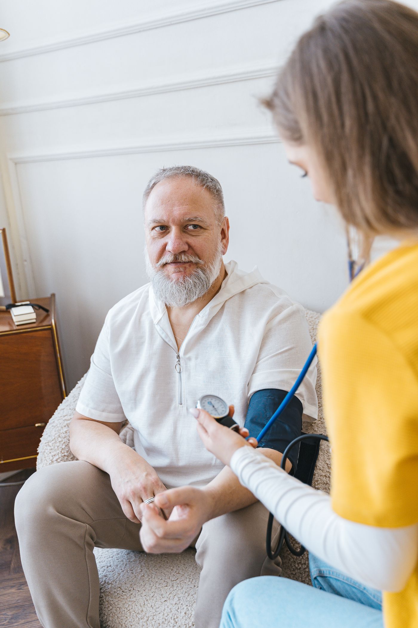 A caregiver checking an older man's blood pressure at home